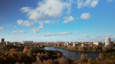 Sonbahar parkında uçuş. Büyük bir gölün kıyısına park et. Ufukta mavi bir gökyüzü ve şehir evleri var. Sarı sonbahar yapraklı ağaçlar görülebilir. Hava fotoğrafçılığı.