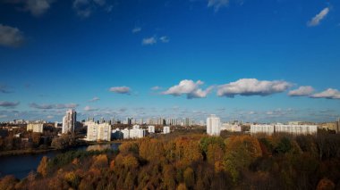 Sonbahar parkında uçuş. Büyük bir gölün kıyısına park et. Ufukta mavi bir gökyüzü ve şehir evleri var. Sarı sonbahar yapraklı ağaçlar görülebilir. Hava fotoğrafçılığı.