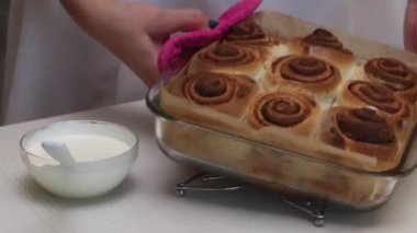 Kadın masaya hazır tarçınlı cam bir form koyar. Bir sonraki konteynırda süsleme için pudra şekerli ekşi krema var. Yakın çekim..