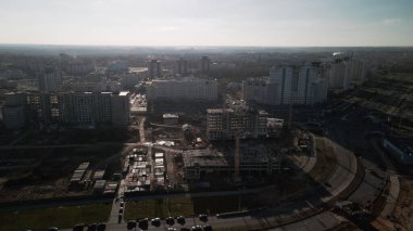 Şehir blokları üzerinde uçuş. Çok katlı binalar ve şantiye. Batan güneşin arka ışığında uçmak. Hava fotoğrafçılığı.