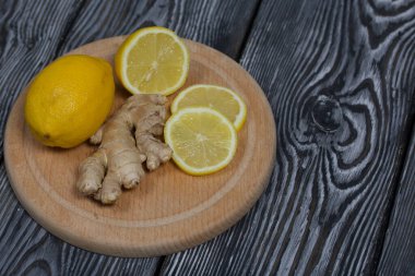 Kesme tahtasında limon ve zencefil. Limon dilimlere ayrılır. Siyah çam ağacından bir arka planda.