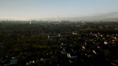 Banliyö batan güneş tarafından aydınlatılır. Evler, bir park alanı ve bir şehir otoyolu görülebilir. Hava fotoğrafçılığı.