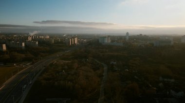 Banliyö batan güneş tarafından aydınlatılır. Evler, bir park alanı ve bir şehir otoyolu görülebilir. Hava fotoğrafçılığı.