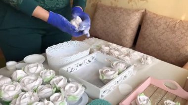 Lastik eldivenli bir kadın ev yapımı şekerlemeleri pudra şekeriyle temizliyor. Önündeki masada çeşitli şekil ve boyutlarda bir zephyr var. Hızlandırılmış çekim. Zaman Uygulaması