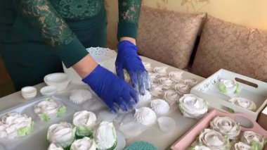 Lastik eldivenli bir kadın ev yapımı şekerlemeleri pudra şekeriyle temizliyor. Önündeki masada çeşitli şekil ve boyutlarda bir zephyr var. Hızlandırılmış çekim. Zaman Uygulaması.