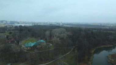 Şehir parkının içindeki nehir. Sonbaharın sonu, bulutlu. Yapraksız ağaçlar ve nehir kıyısında kurumuş sazlıklar. Şehir ufukta görünüyor. Hava fotoğrafçılığı.
