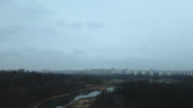 Şehir parkının içindeki nehir. Sonbaharın sonu, bulutlu. Yapraksız ağaçlar ve nehir kıyısında kurumuş sazlıklar. Şehir ufukta görünüyor. Hava fotoğrafçılığı.