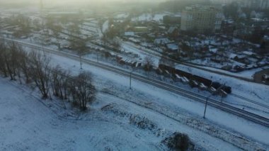Şehir üzerinde uçuş. Kış şehri manzarası. Yakınlarda bir demiryolu hattı var. Sisli bir sis görünür. Hava fotoğrafçılığı.