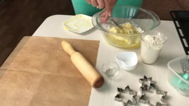Bir kadın konteynırda bisküvi yapmak için gereken malzemeleri karıştırıyor. Marshmallow sandviçi pişiriyorum. Malzemeler ve aletler masaya serildi.