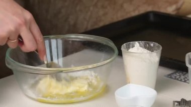 Bir kadın konteynırda bisküvi yapmak için gereken malzemeleri karıştırıyor. Marshmallow sandviçi pişiriyorum. Malzemeler ve aletler masaya serildi. Yakın çekim.