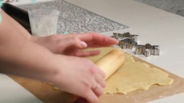 Bir kadın bisküvi hamurunu merdaneyle yuvarlıyor. Marshmallow sandviçi pişiriyorum. Yanında da kar tanesi şeklinde hamur için bir form var. Yakın çekim..