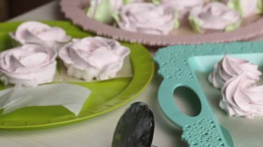 Bir kadın hamur işi torbasıyla marşmelov güllerinde taç yaprakları yapıyor. Farklı şekillerde şekerlemeler tepsilerin üzerine serilmiştir. Yakından çekilmiş...