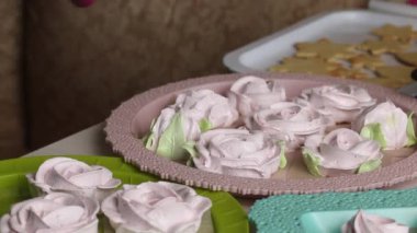 Bir kadın hamur işi torbasıyla marşmelov güllerinde taç yaprakları yapıyor. Farklı şekillerde şekerlemeler tepsilerin üzerine serilmiştir. Yakından çekilmiş..