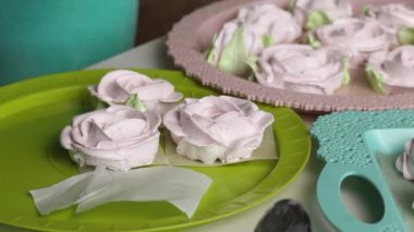 Bir kadın hamur işi torbasıyla marşmelov güllerinde taç yaprakları yapıyor. Farklı şekillerde şekerlemeler tepsilerin üzerine serilmiştir. Yakından çekilmiş.