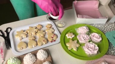 Bir kadın şekerli sandviçleri şekerle süslüyor. Değişik şekil ve boyutlarda şekerlemeler. Şekerleme gülleri. Şekerlemeler masanın üzerine yayılmış..