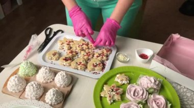 Kadın marşmelovlu sandviç hazırlıyor. Onları şekerlerle süslüyor. Hazır tatlılar masaya serilmiştir.