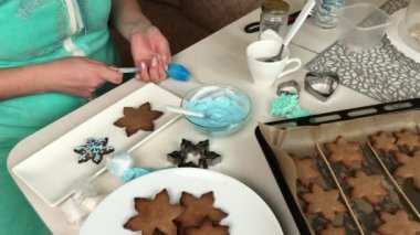Bir kadın zencefilli ekmeği süslemek için bir pasta torbasını kremayla dolduruyor. Yakınlarda kar taneleri şeklinde zencefilli ekmekler var. Genel plan.