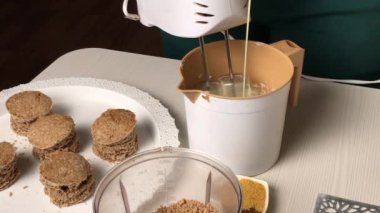 Bir kadın yağlı kremaya konsantre süt ekler. Bisküvi kırıntılı bisküvi keki için. Genel plan.