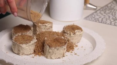 Bir kadın tereyağlı kremalı pandispanya yapar. Kekleri bisküvi kırıntılarına batırıyor. Yakın plan..