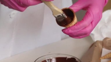 Bir kadın waffle külahlarına sıvı çikolata sürüyor. Çikolata ve lokumla boynuz yapıyor. Yakın plan..