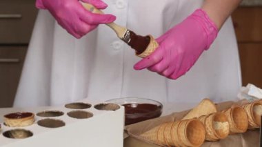 Bir kadın waffle külahlarına sıvı çikolata sürüyor. Çikolata ve marşmelovla boynuz yapar