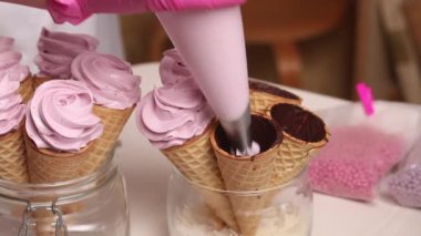 Bir kadın waffle külahlarını şekerle dolduruyor. Pasta torbasıyla. Yakın plan.