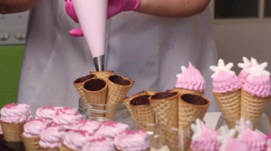 Bir kadın waffle külahlarını şekerle dolduruyor. Pasta torbasıyla. Ortam planı.