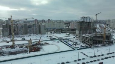 Modern bir şehir bloğunun inşaat alanı. Yüksek binalar yapım aşamasında. İnşaat kulesi vinçleri. Kışın inşaat alanında. Gün batımında hava fotoğrafçılığı.