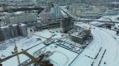 Modern bir şehir bloğunun inşaat alanı. Yüksek binalar yapım aşamasında. İnşaat kulesi vinçleri. Kışın inşaat alanında. Gün batımında hava fotoğrafçılığı.