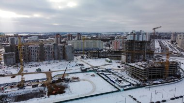 Modern bir şehir bloğunun inşaat alanı. Yüksek binalar yapım aşamasında. İnşaat kulesi vinçleri. Kışın inşaat alanında. Gün batımında hava fotoğrafçılığı.