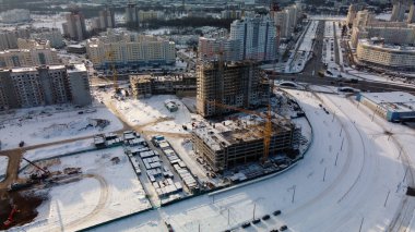 Modern bir şehir bloğunun inşaat alanı. Yüksek binalar yapım aşamasında. İnşaat kulesi vinçleri. Kışın inşaat alanında. Gün batımında hava fotoğrafçılığı.