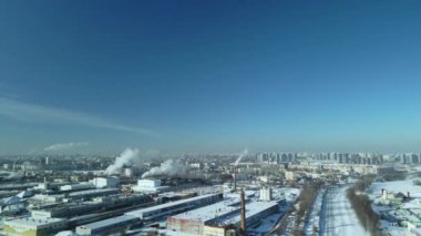 Karla kaplı fabrika binaları. Fabrika duman bacaları. Yakınlarda bir demiryolu var. Şehir bloklarını görebilirsin. Kış endüstriyel manzarası. Hava fotoğrafçılığı.