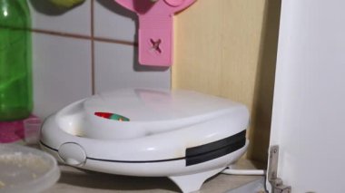 Bir kadın ısıtılmış waffle ızgarasını açar ve waffle 'ın hazır olup olmadığını kontrol eder. Gözleme ızgarasını kapatır. Kahvaltı hazırlığı. Yakın plan.