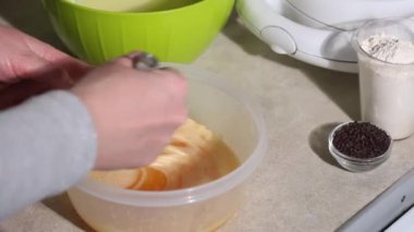 Bir kadın waffle hamuru hazırlar. Malzemeleri karıştırıyor. Yanında bir waffle ızgarası var. Yakın plan..