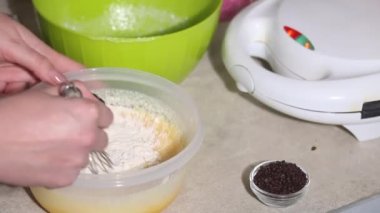 Bir kadın waffle hamuru hazırlar. Malzemeleri karıştırıyor. Yanında bir waffle ızgarası var. Yakın plan.
