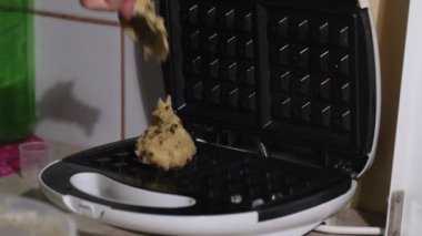 Bir kadın çikolatalı hamuru ısıtılmış waffle ızgarasına koyar. Pişirmek için waffle ızgarasını kapatır. Kahvaltı hazırlığı. Yakın plan..