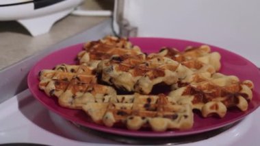 Bir kadın elektrikli gözleme ızgarasında waffle yapmaya hazır olup olmadığını kontrol eder. Tabakta taze yapılmış waffle 'lar. Kahvaltı hazırlığı. Yakın plan..