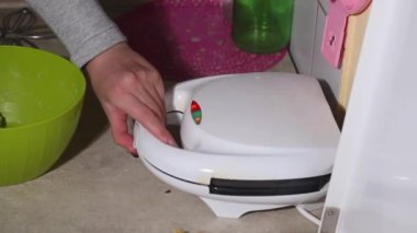 Bir kadın elektrikli waffle ızgarasını açar ve waffle pişirme derecesini kontrol eder. Kahvaltı hazırlığı. Yakın plan..