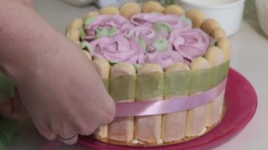 Bir kadın pasta süslemek için kurdele bağlıyor. Pasta marşmelov gülleriyle süslenmiş. Savoiardi kurabiyeli kek ve marshmallow gülleri. Yakın plan..