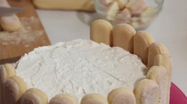 Bir kadın pastayı Savoiardi kurabiyeleriyle kaplıyor. İçinde Savoiardi kurabiyeleri ve marshmallow gülleri olan kek. Yakın plan..