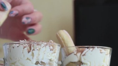 Bir kadın bardakta tatlı yapar. İçine Savoyardi kurabiyeleri koyuyor. Savoiardi kurabiyesi ve kremalı tatlı. Tiramisu kurabiyeleri. Yakın plan..