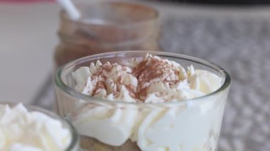 Bir kadın bardakta tatlı yapar. Kakao tozu serpin. Savoiardi kurabiyesi ve kremalı tatlı. Tiramisu kurabiyeleri. Yakın plan..