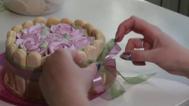 Bir kadın pastayı kurdeleyle bağlıyor. İçinde Savoiardi kurabiyeleri ve marshmallow gülleri olan kek.