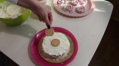 Bir kadın kurabiye kekini istifliyor. İçinde Savoiardi kurabiyeleri ve marshmallow gülleri olan kek...