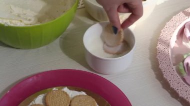 Bir kadın kurabiye kekini istifliyor. İçinde Savoiardi kurabiyeleri ve marshmallow gülleri olan kek..