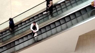 Bloomington, Minnesota 'da. 24 Nisan 2022. Erkek, Amerika 'daki alışveriş merkezinin farklı katlarında yürüyen merdivenlerde kadınlara sarılıyor..