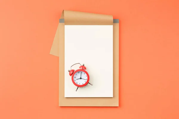 Cuaderno abierto y despertador sobre fondo naranja — Foto de Stock