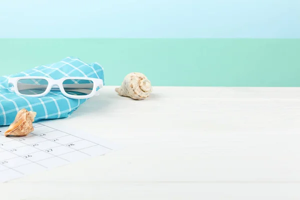 Vacation calendar at the sea on white wooden background. Summer holiday concept. Decoration of starfish and seashells. Sunglasses with shorts side view.