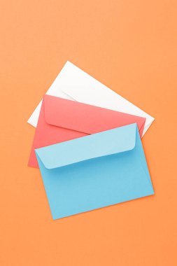 Multicolored paper mail envelopes on orange isolated background. Top view, copy space.