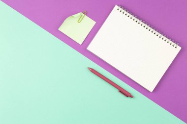 Beyaz kalemle, not kağıdıyla ve iki renk arkaplan üzerine klips ile spiral defter aç. Üst manzara, düz uzanma.